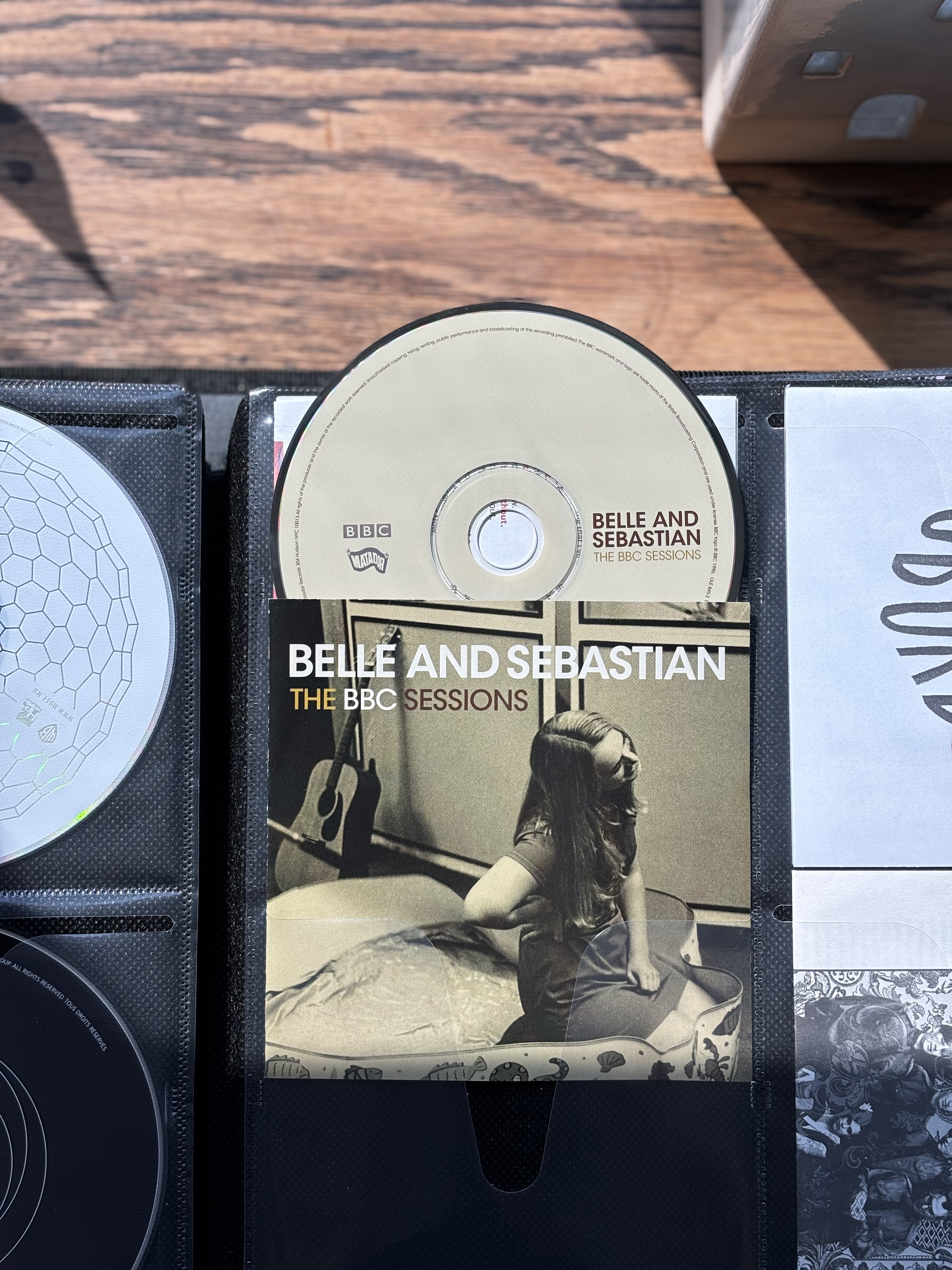 The cover of Belle and Sebastian's album "The BBC Sessions" showing a young woman sitting on the floor, a guitar in the background. 