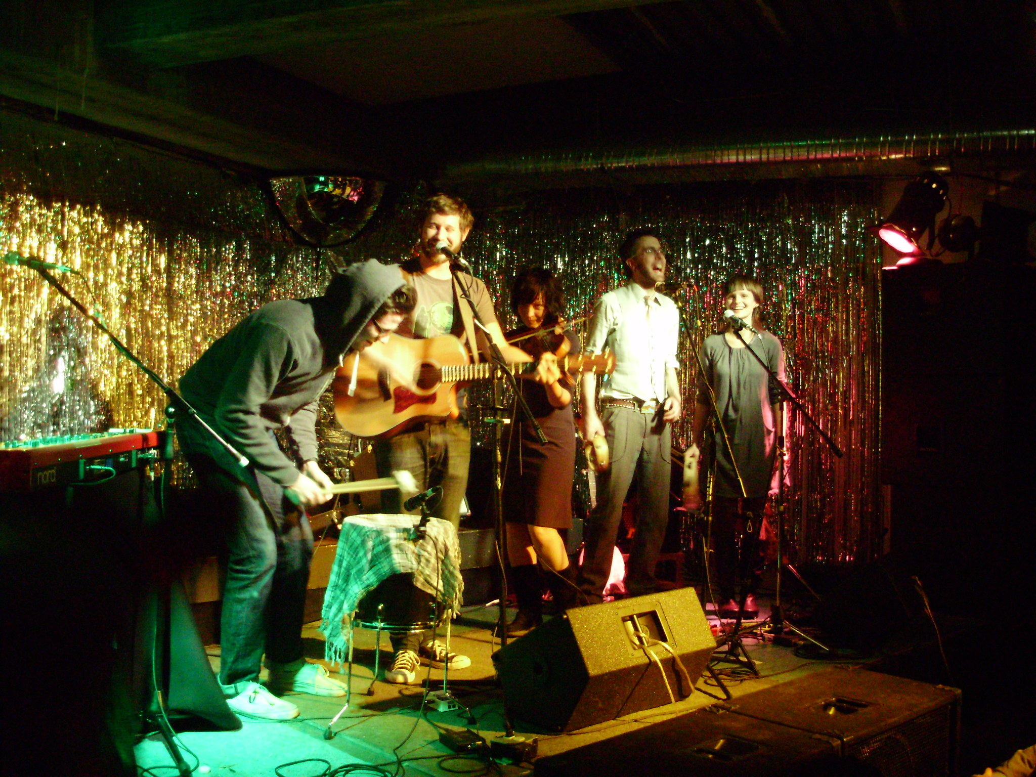 Group of musicians standing on stage, with a ribbony metallic background